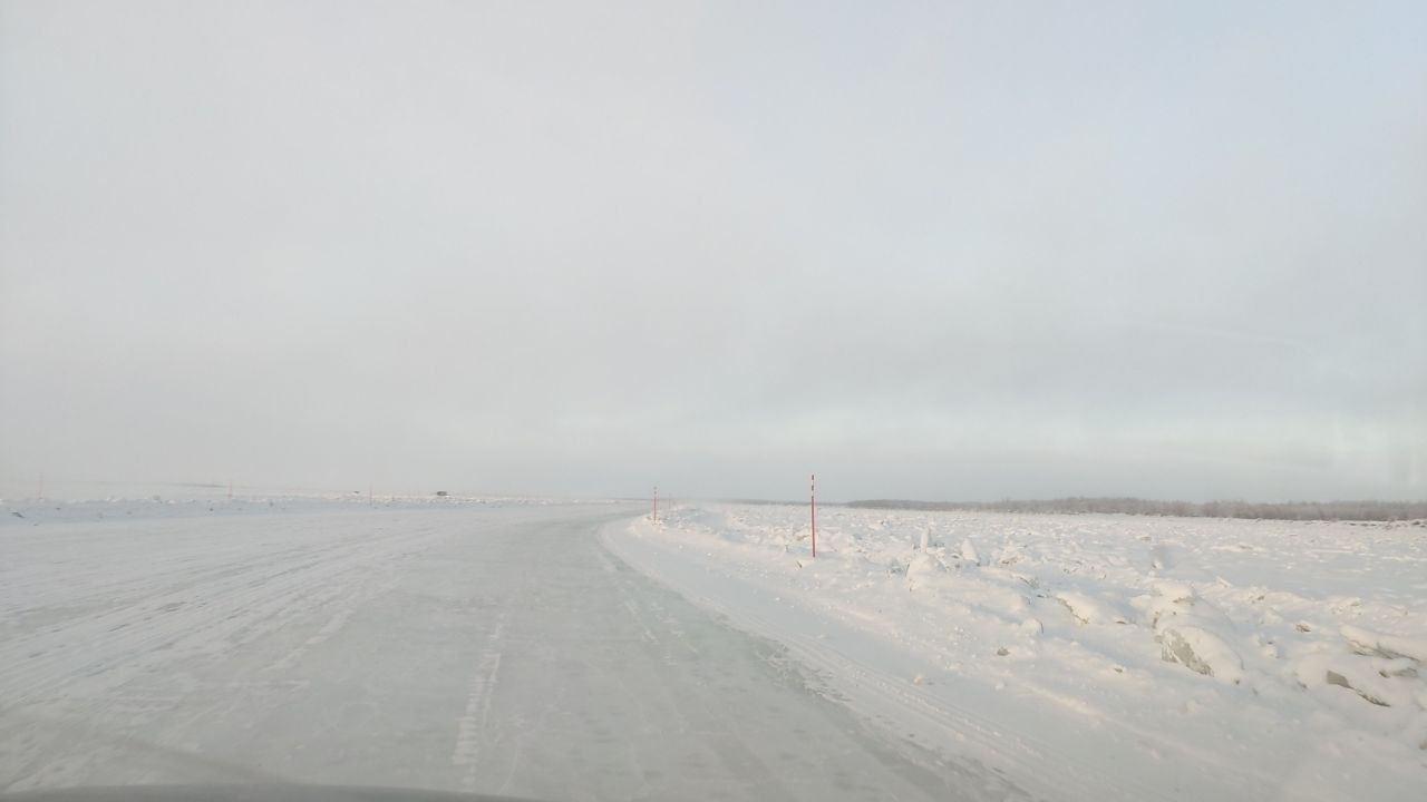 Snowy road stretching into a foggy, overcast landscape with snowbanks along the side.
