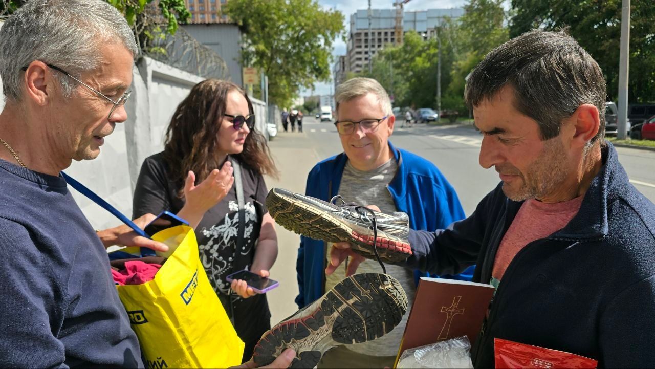 People outdoors examining a large bird while talking on a sunny street.