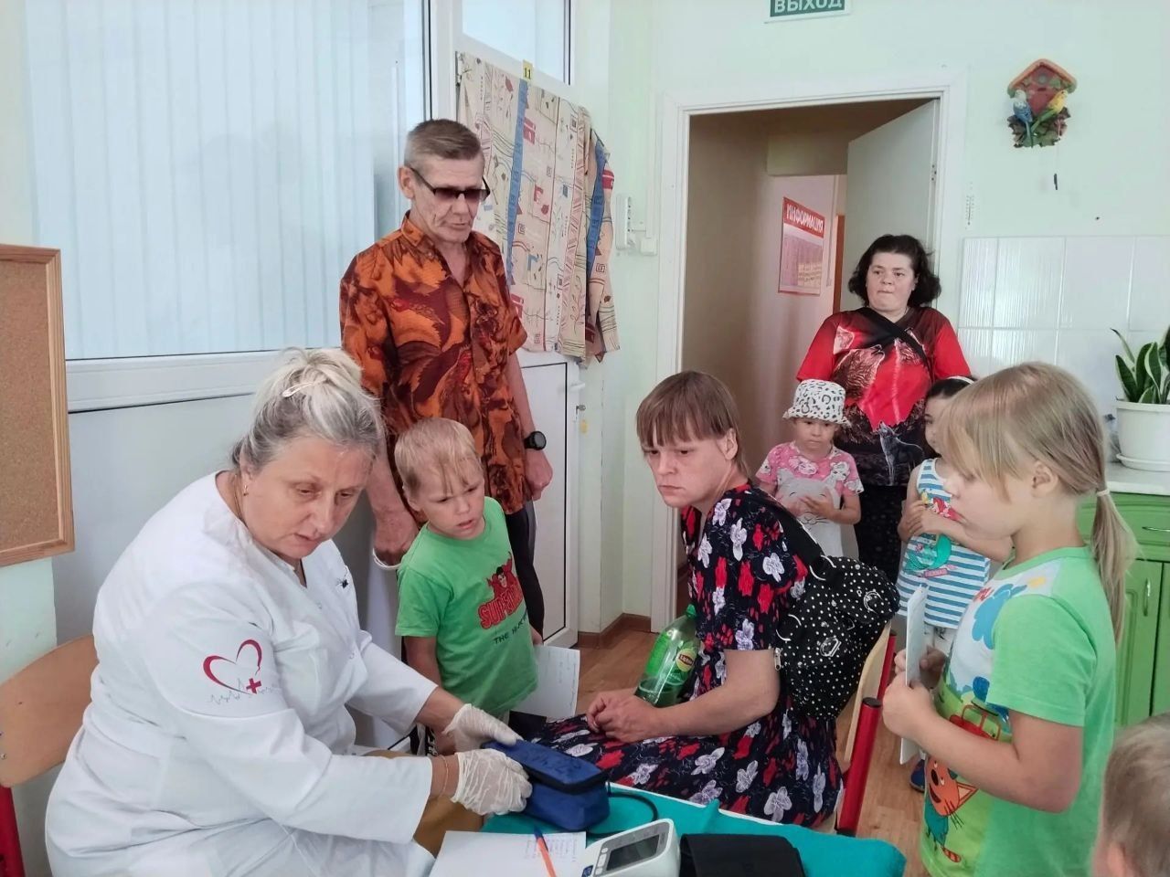 People gathered around a table as a woman in a white coat assists with an activity indoors.