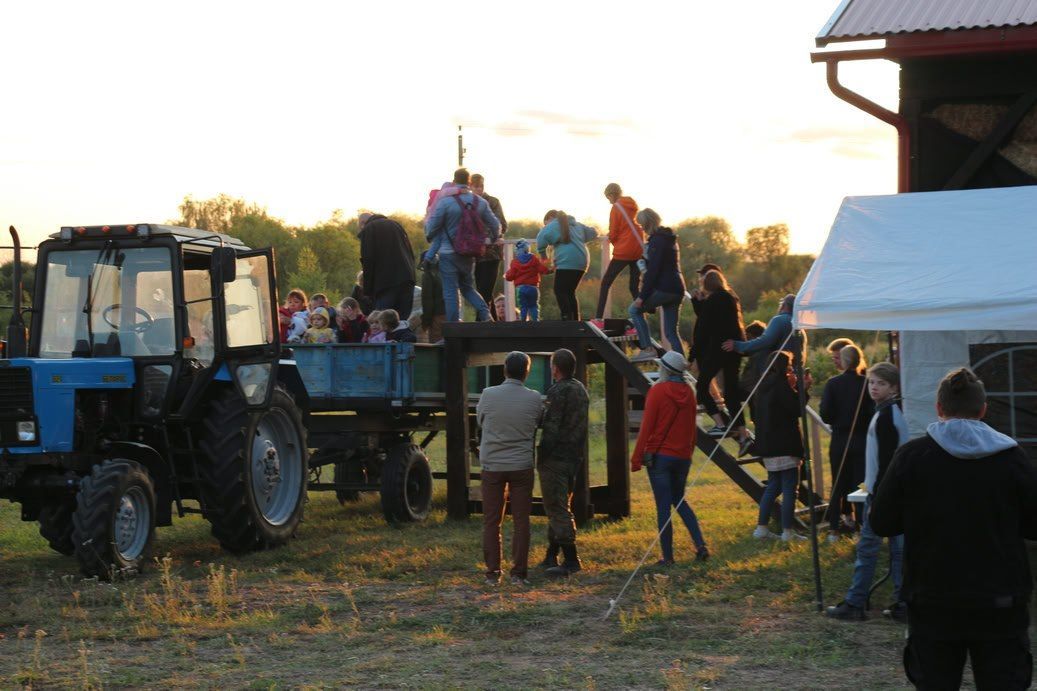 People standing on and around a tractor trailer in a field at sunset, near a white tent.