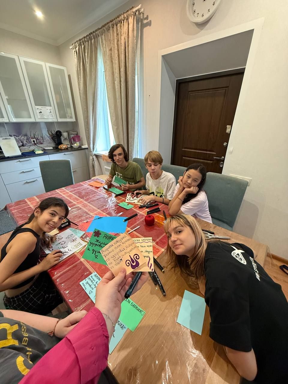 Friends sitting around a dining table crafting colorful paper designs in a bright kitchen