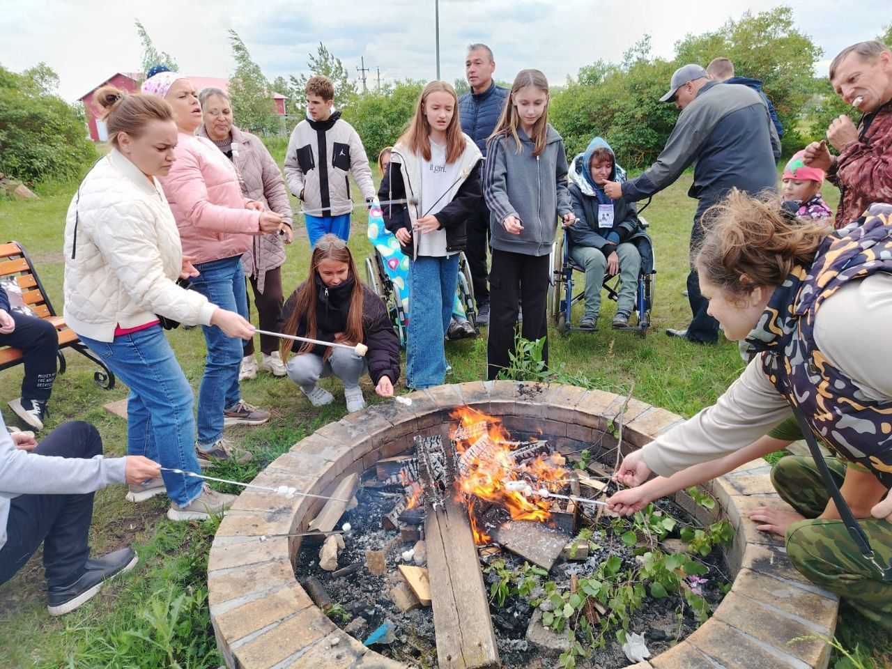 People gathered around a fire pit outdoors, tending a small bonfire with sticks.