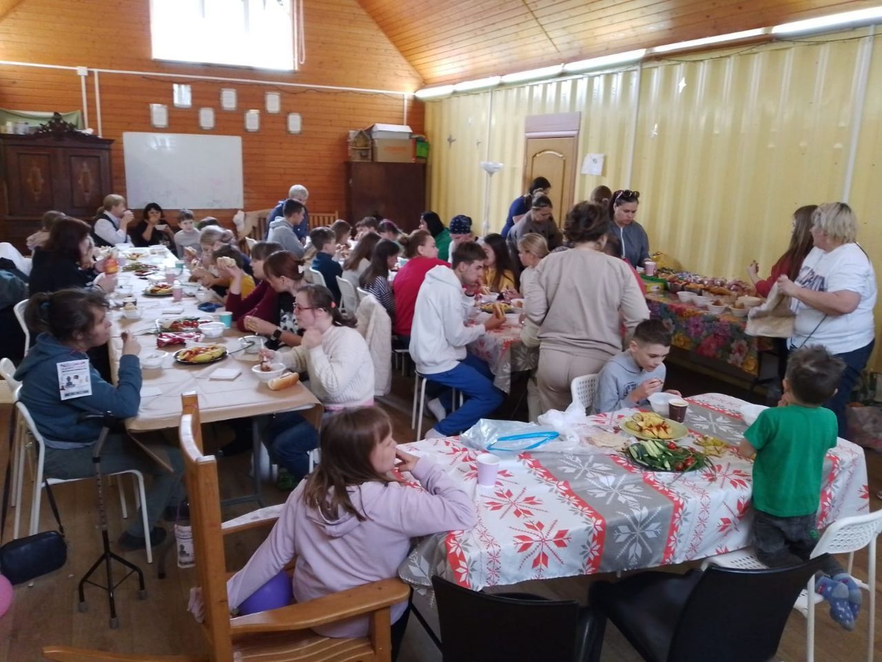 People gathered around long tables in a wood-paneled hall, sharing a meal and conversation.
