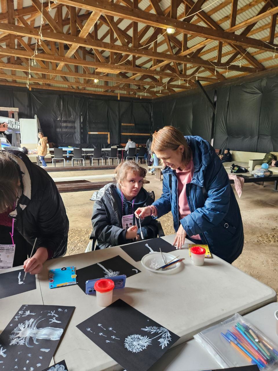 People working at a table in a rustic workshop, arranging black paper prints and craft supplies.