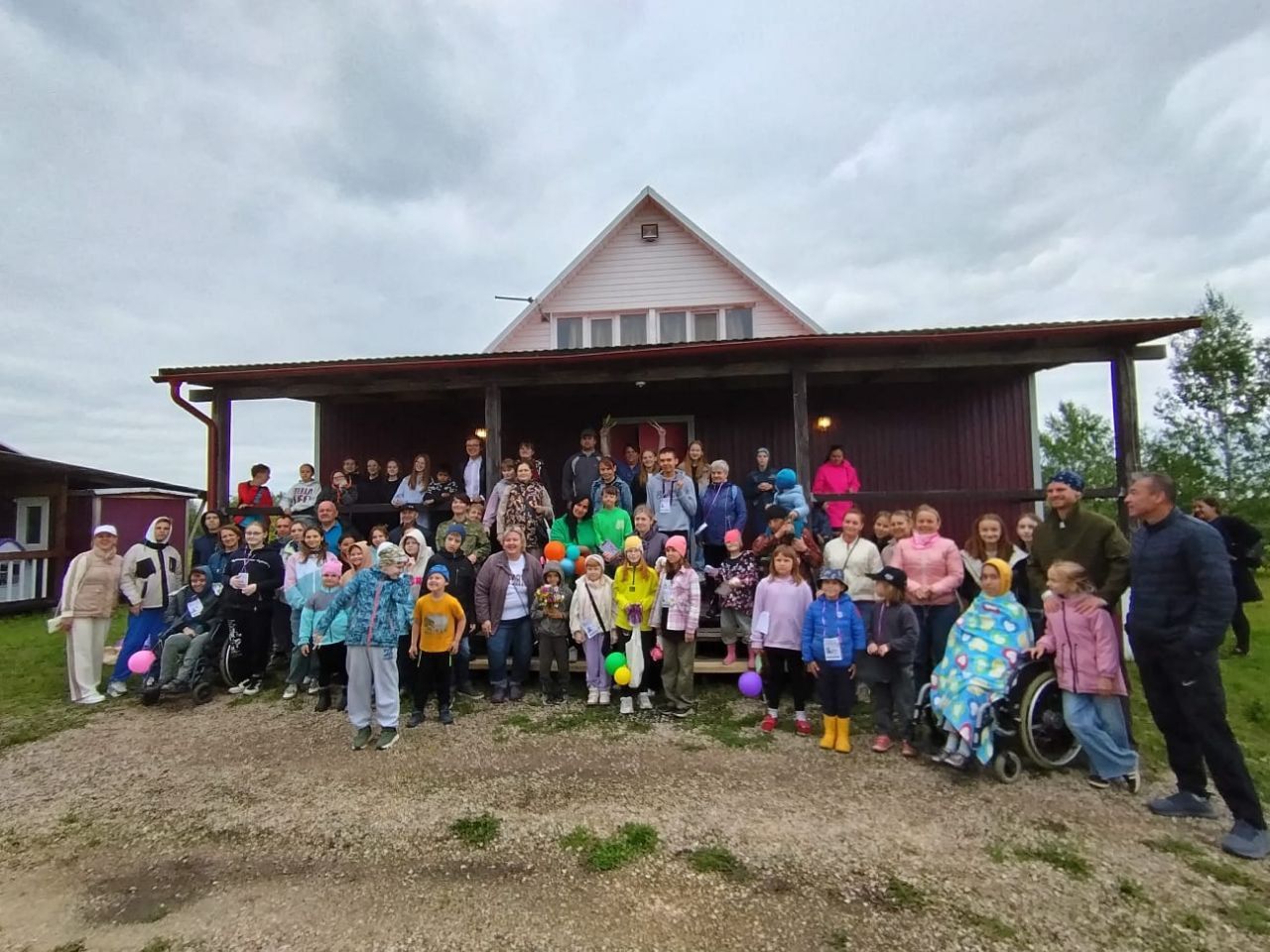 Large group posing on the porch of a rustic house under a cloudy sky