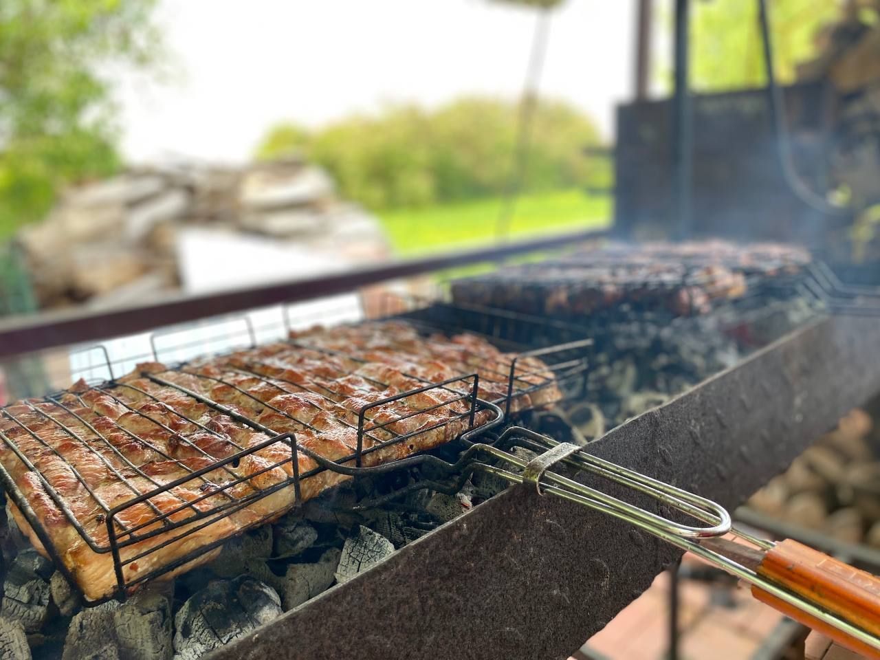 Grilled meat on a barbecue over hot coals with smoke rising, outdoors on a sunny day