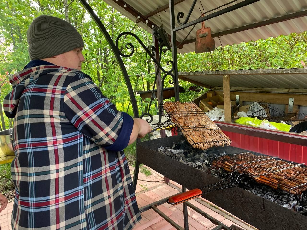 Person grilling skewers over a charcoal fire under a covered outdoor shelter