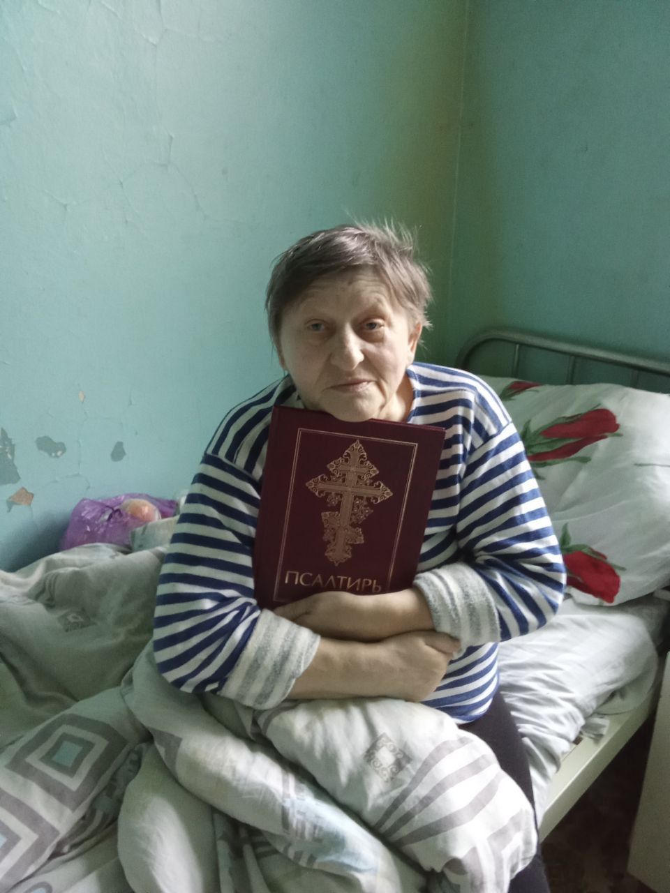 Person sitting on a bed, holding a red book, in a sparse room with green walls.