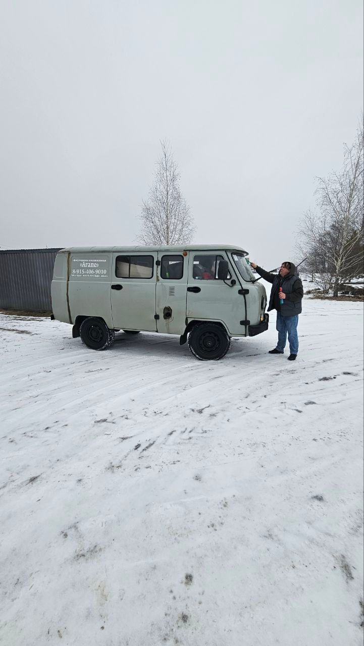 Person standing by a light green van in a snowy outdoor lot, reaching toward the front door.