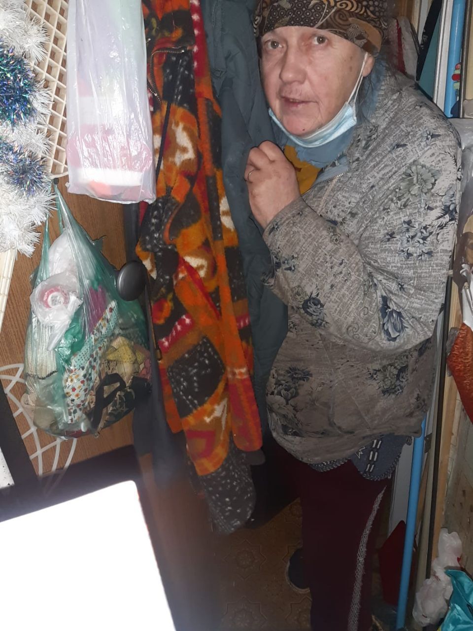 Person in a patterned coat standing in a narrow shop aisle beside hanging colorful scarves and bags.