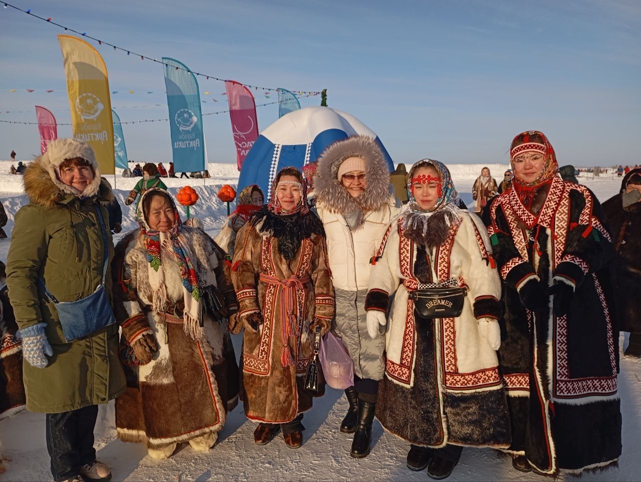 Group of people in colorful winter clothing posing outdoors in snow with tall festive banners behind them