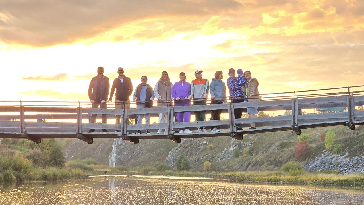 Group standing on a bridge over water at sunset, with golden light and trees in the background