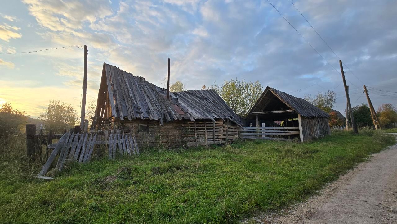 Rustic wooden farm buildings with weathered roofs beside a dirt road at sunset