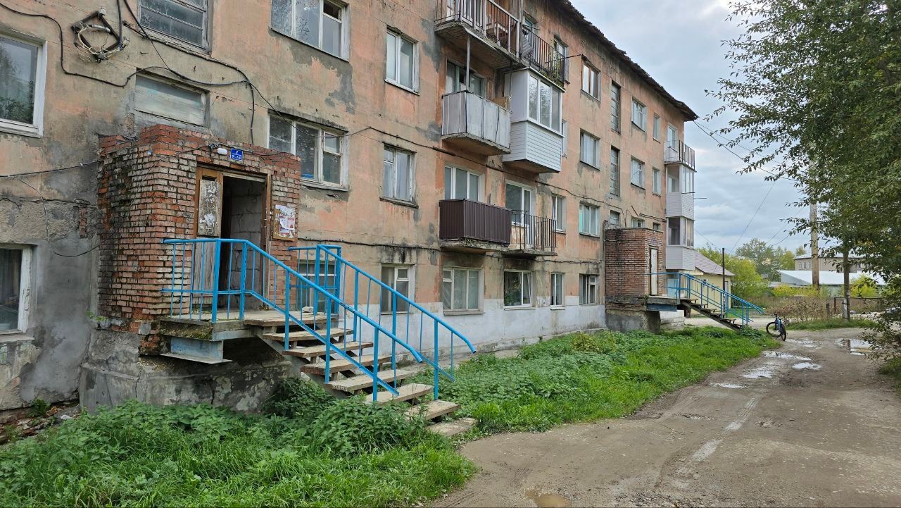 Deteriorating apartment building with blue metal stairs and a muddy path beside it