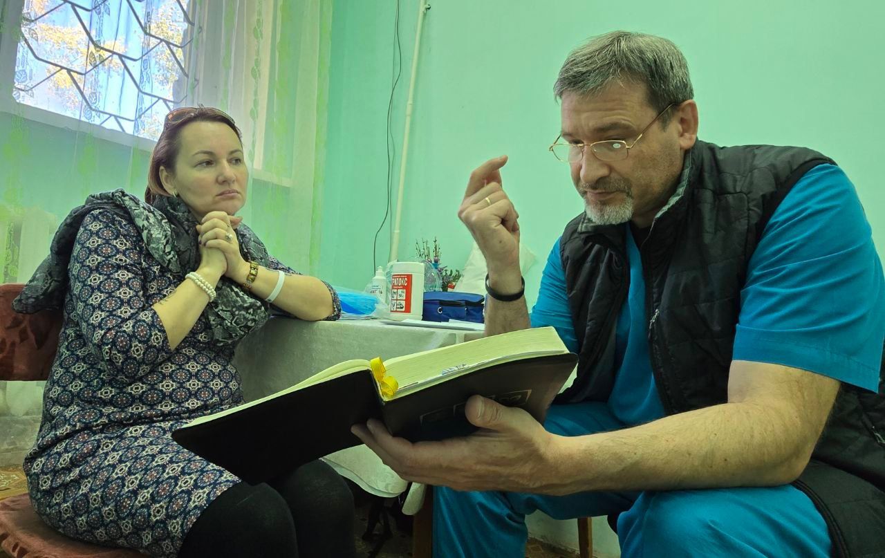 Two people in a room discussing a large open book at a table