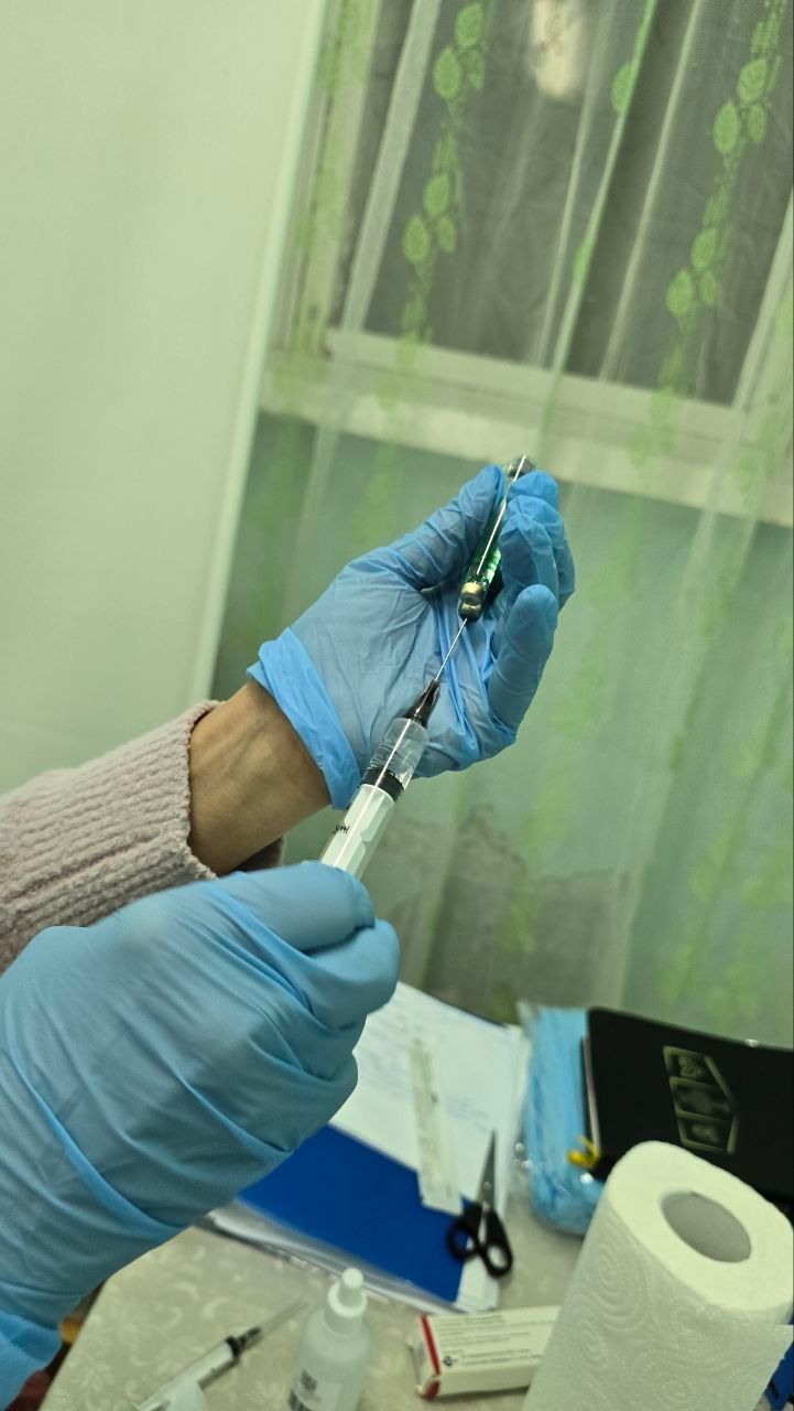 Gloved hands hold a syringe and small vial over a lab table with a paper towel roll and notebook