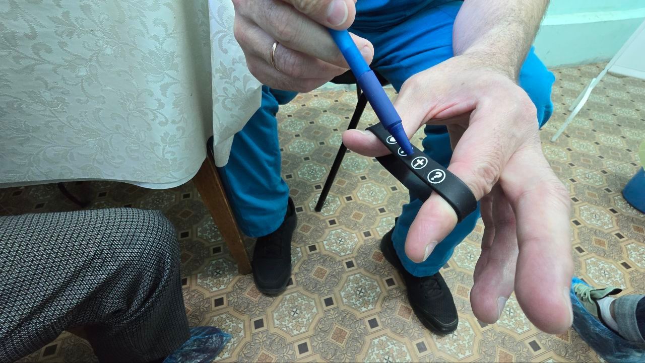Hands using blue-handled pliers to cut a black cable on a tiled floor.