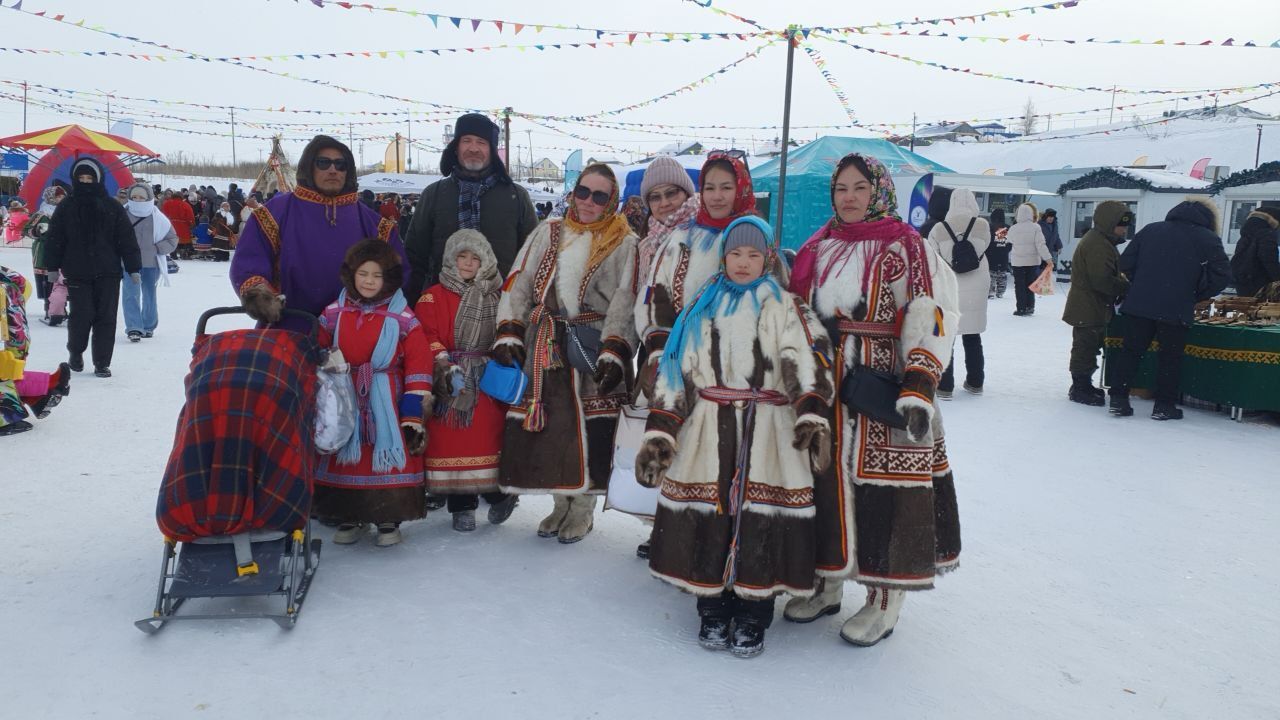 Group posing in colorful winter clothing at an outdoor snowy festival with festive lights and tents