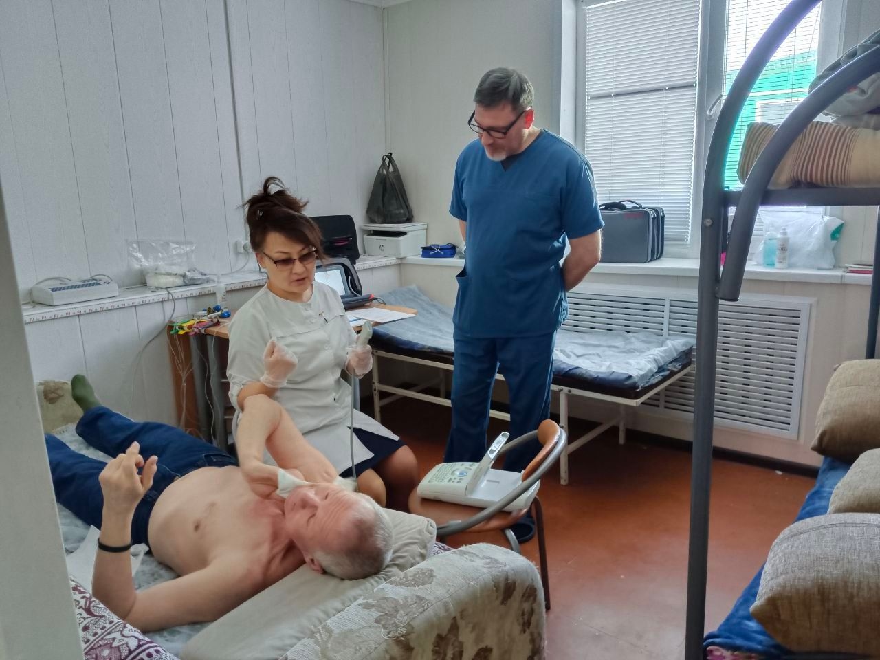 Medical treatment in a clinic room, with a patient on an exam table and two caregivers nearby