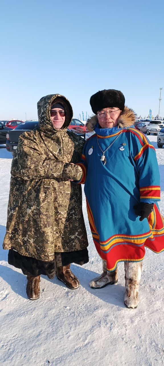 Two people in winter coats standing together in the snow with a frozen landscape behind them