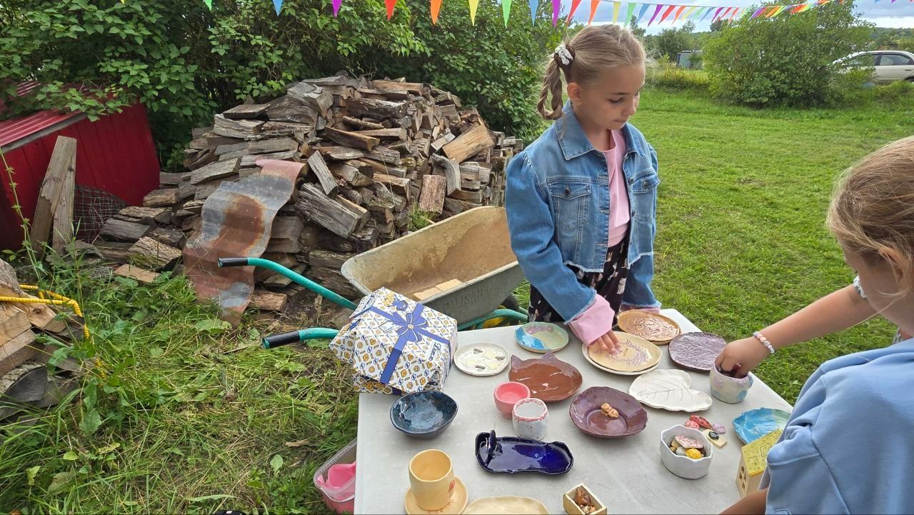 Two children painting at a table outdoors with cups of colorful paint and craft supplies