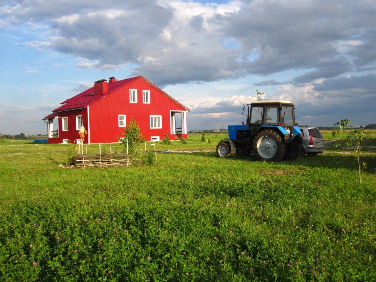 Red farmhouse in a green field with a blue tractor under a cloudy sky