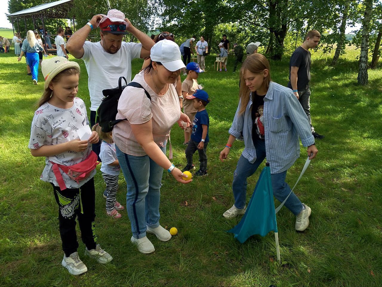 Children and adults playing a lawn game outdoors, aiming balls across a grassy park