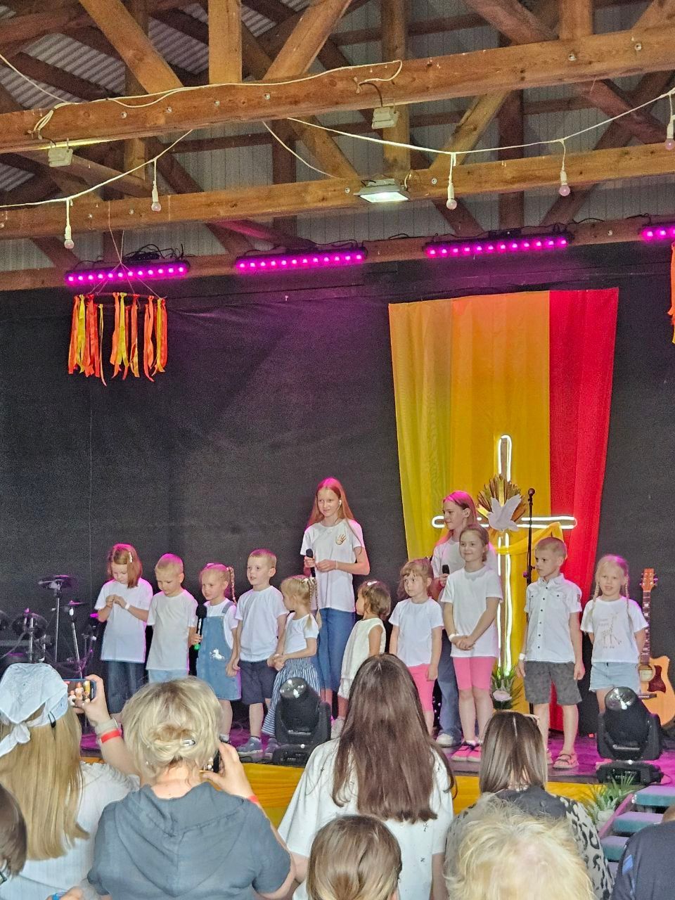 Children performing onstage under colorful lights with a gold cross and red-yellow backdrop