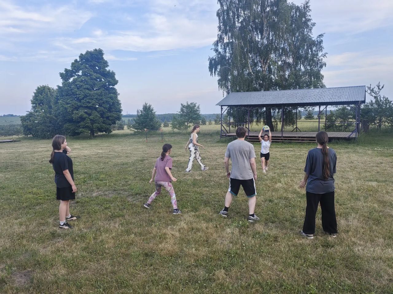 People standing in a grassy field near a pavilion, as if playing a group game.