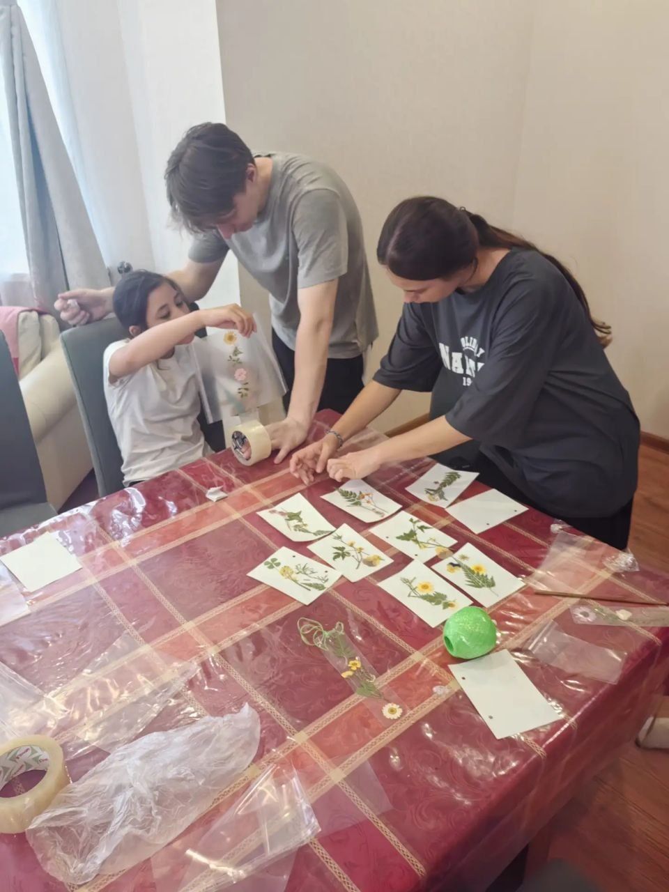 Three people arranging paper bills on a red tablecloth indoors