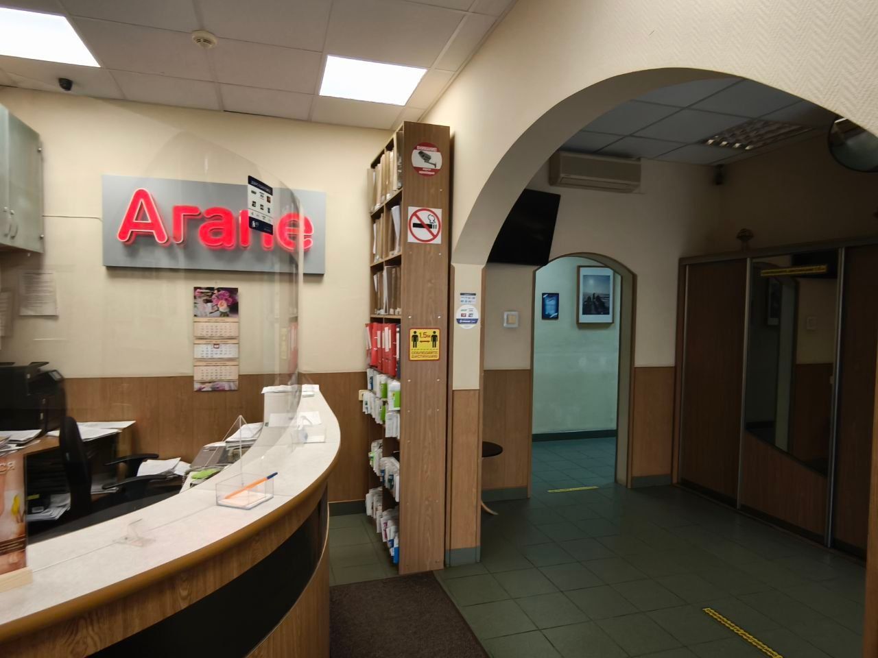 Clinic reception desk with glowing red sign, hallway archway, and brochure display in a beige lobby