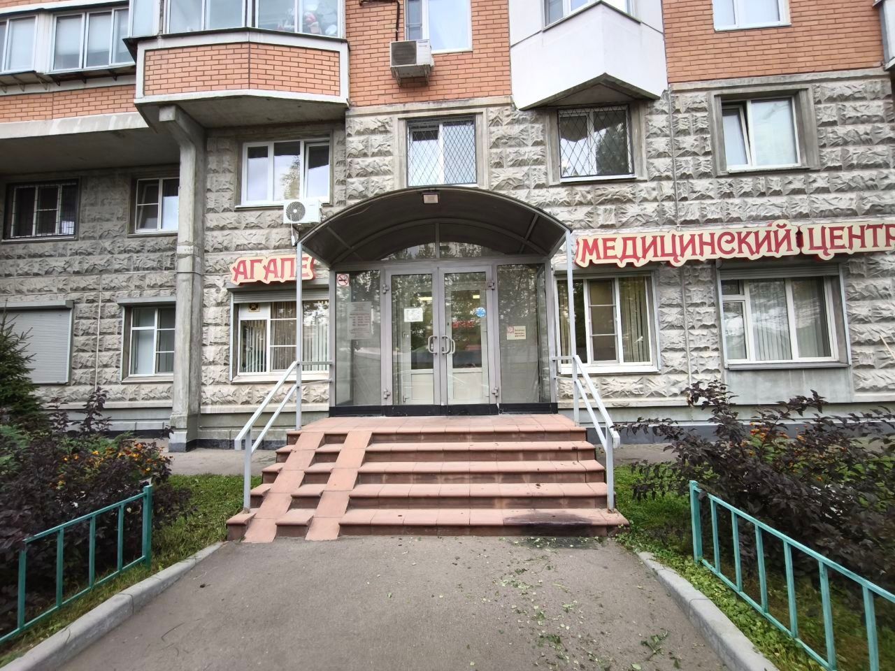 Entrance to a medical center building with stairs, glass doors, and red Russian signage