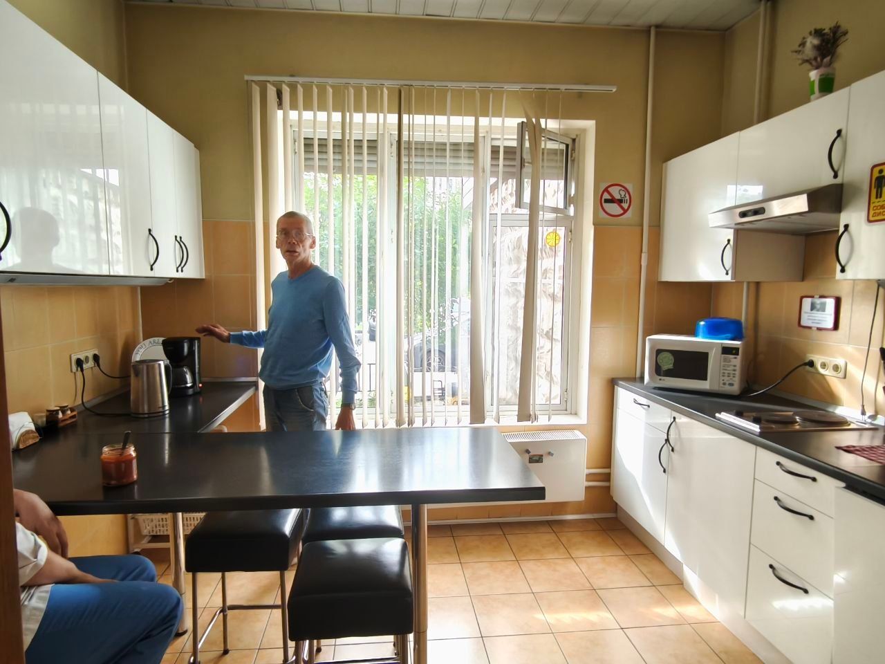 Man standing in a bright kitchen near the counter and table, with white cabinets and a glass door to the patio