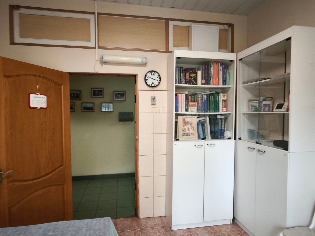 Small office room with open door, wall clock, and white bookshelves filled with books and papers.