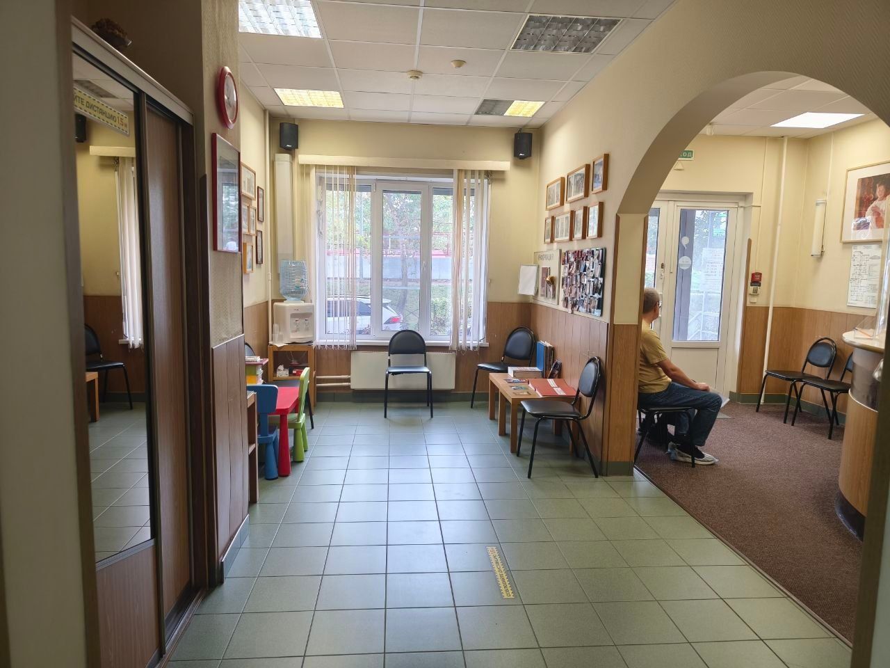 Long hallway with chairs, tables, wall photos, and a window at the end.