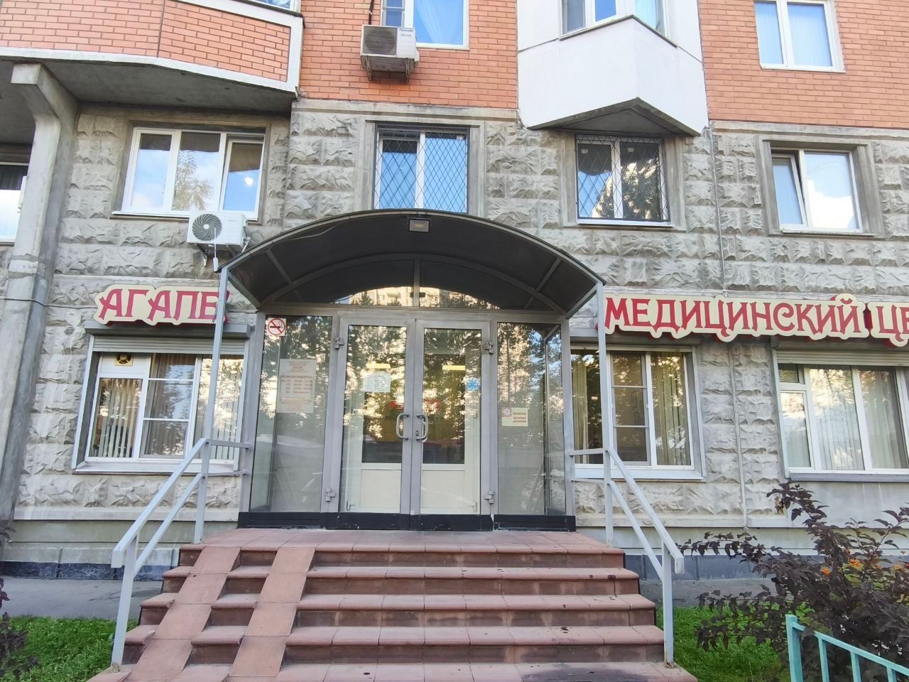 Entrance to a medical clinic with steps, glass doors, and red Cyrillic signage above the windows
