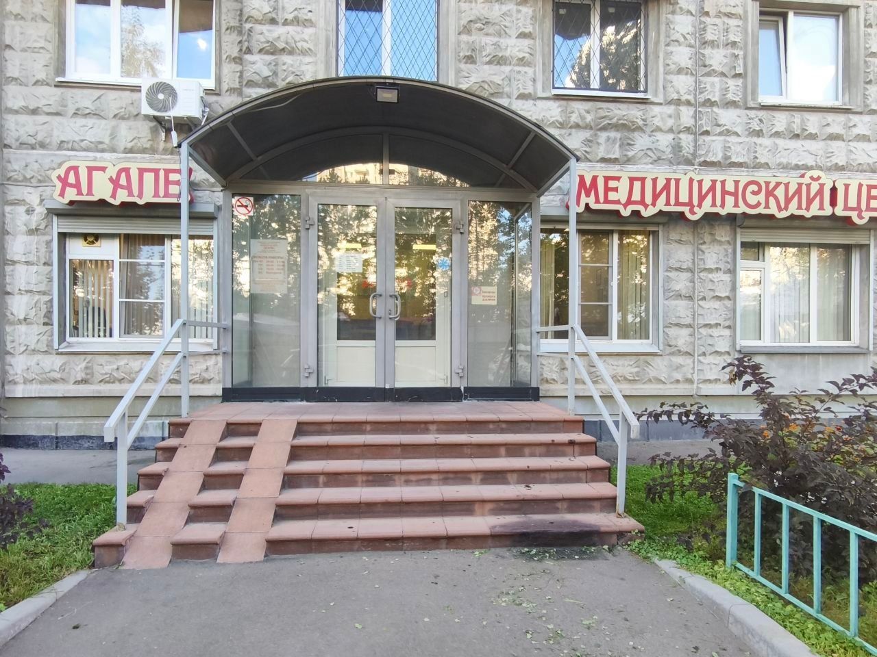 Front entrance of a medical center with glass doors, steps, and red Cyrillic signage on a stone building