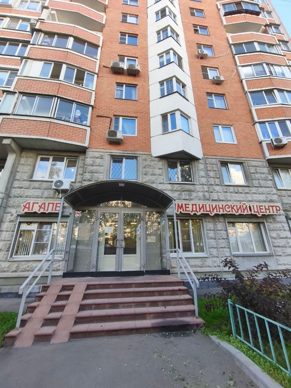 Entrance of a red-brick medical center apartment building with stairs and glass doors