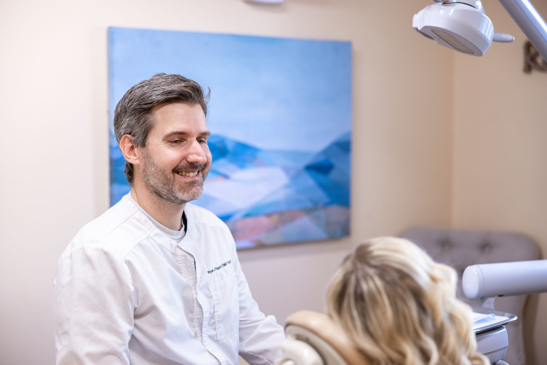 A dentist is smiling while talking to a patient in a dental chair.