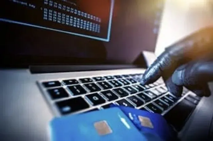Gloved hand typing on a laptop beside a blue credit card, suggesting online payment or fraud