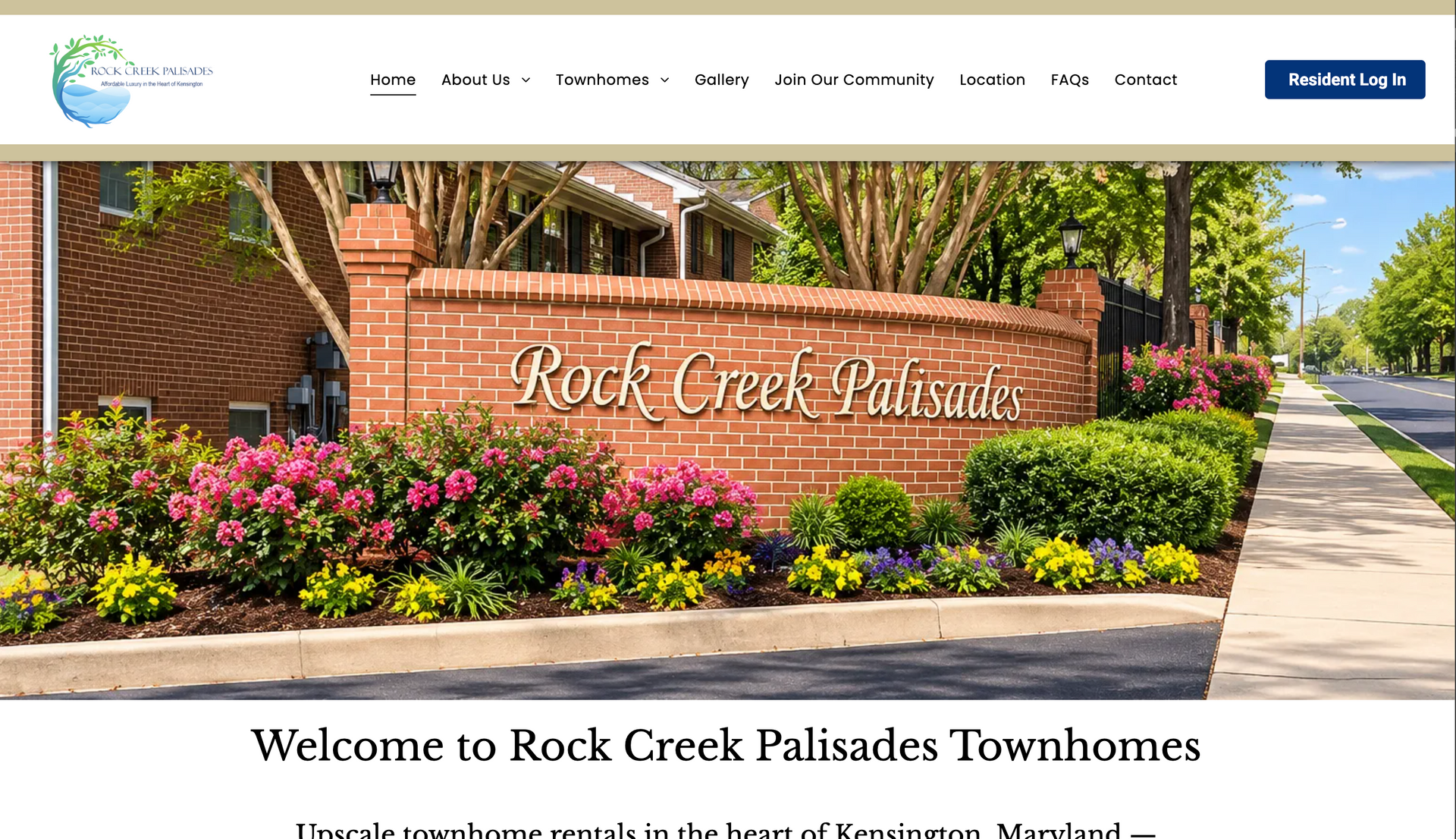 Rock Creek Palisades Townhomes entrance with brick sign, flowers, and sidewalk under bright sun