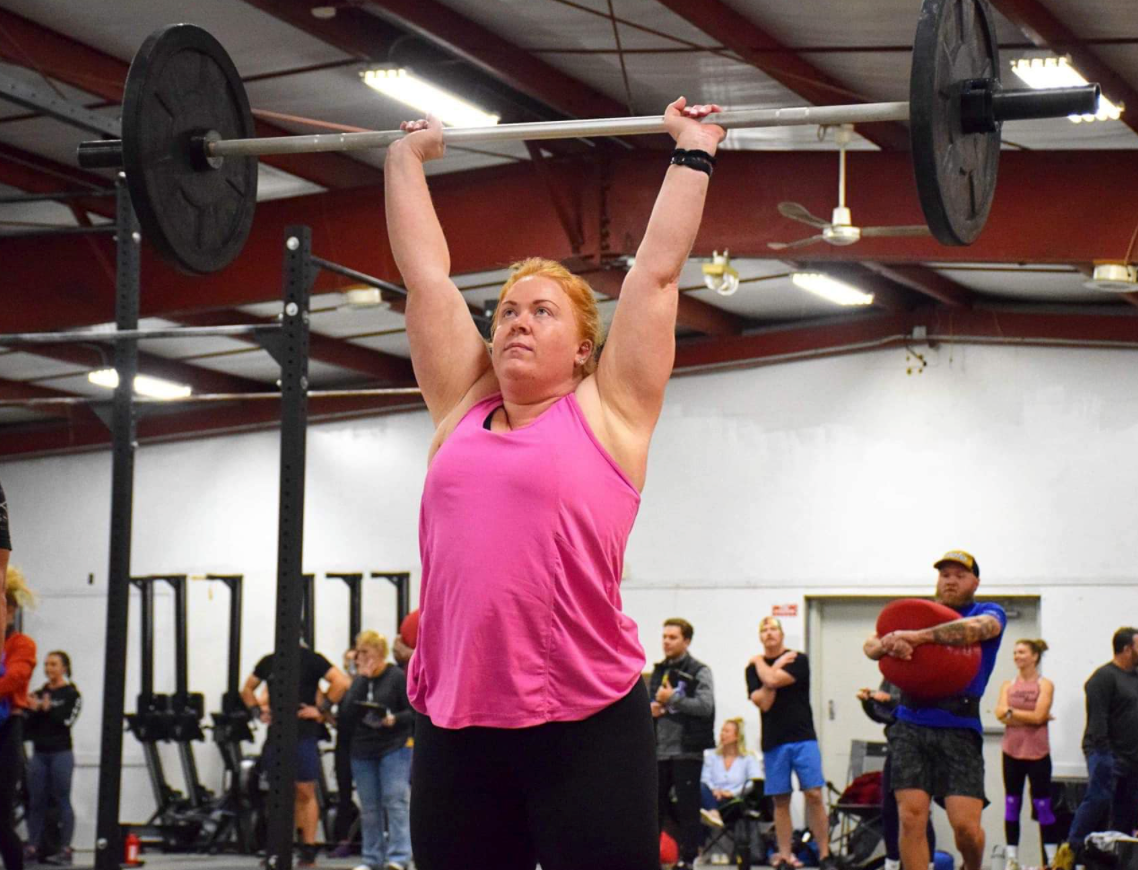 A woman is lifting a barbell over her head in a gym.