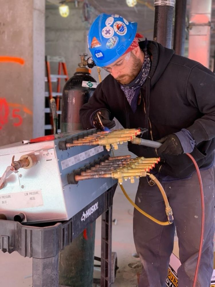 Construction worker in blue hard hat soldering copper pipes, using torch.