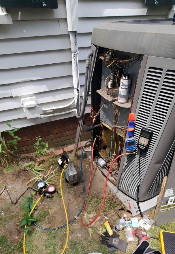 Technician uses gauges to check an air conditioner outside a brick building.