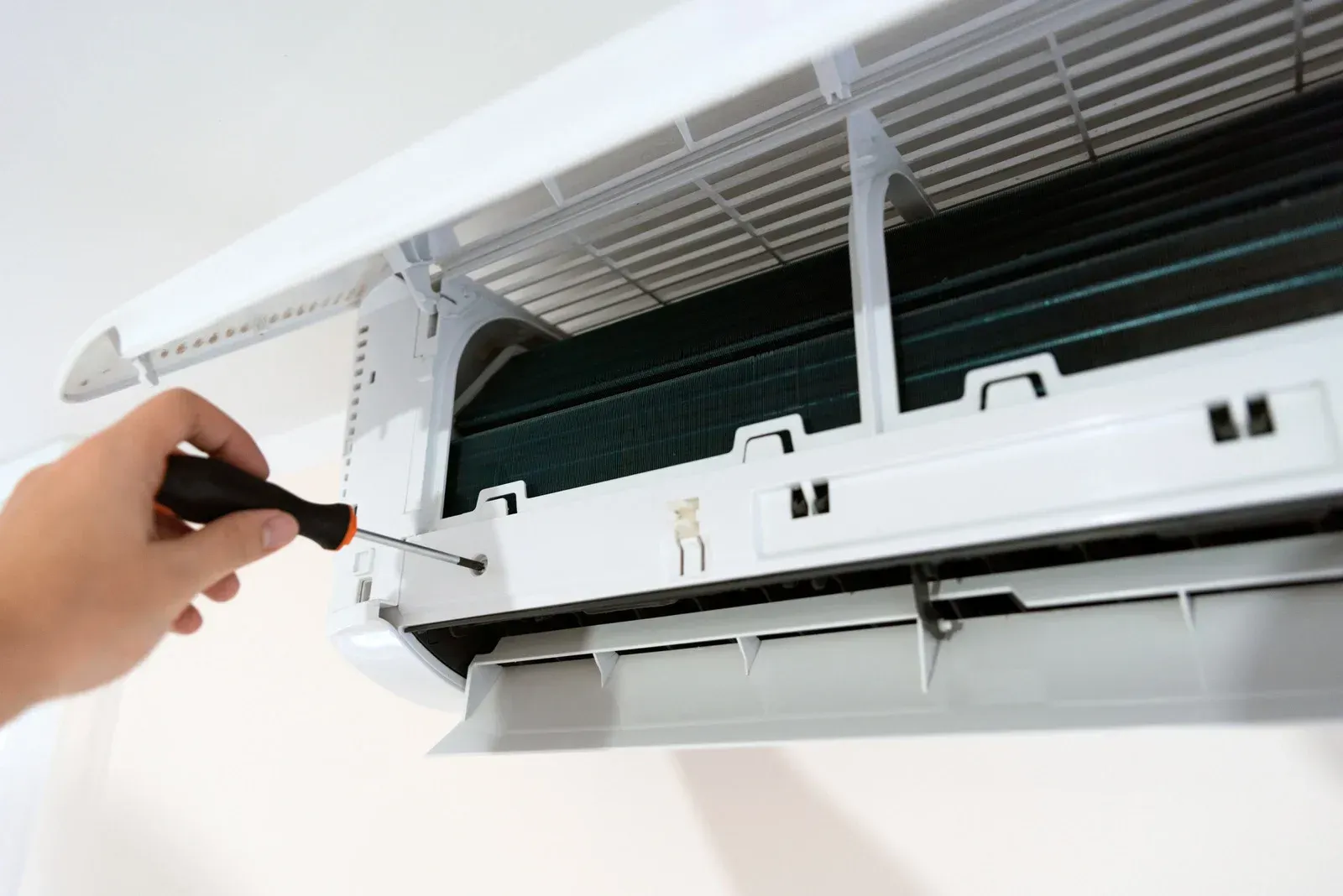 Person using a screwdriver to open an air conditioner for maintenance.