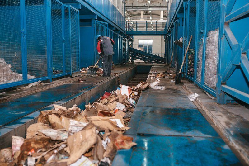 Un operaio smista i rifiuti su un nastro trasportatore blu in un impianto di riciclaggio industriale.