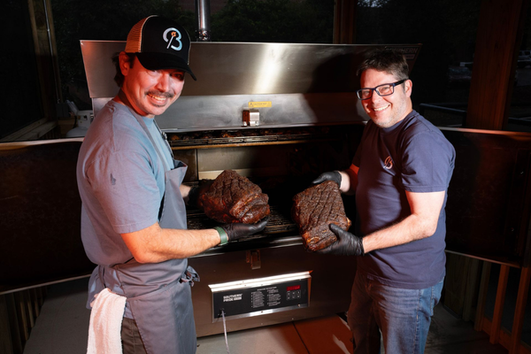 Founders of Brookshire BBQ holding freshly smoked brisket in front of the smoker