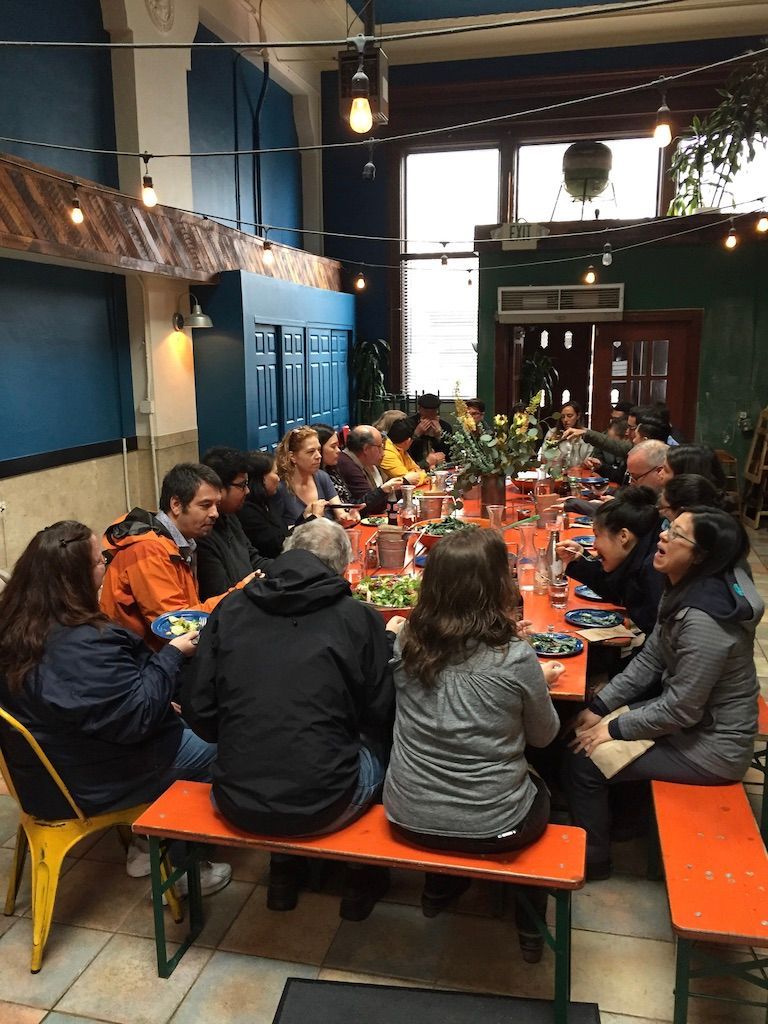 People seated around a long table in a colorful indoor dining room, sharing a meal.