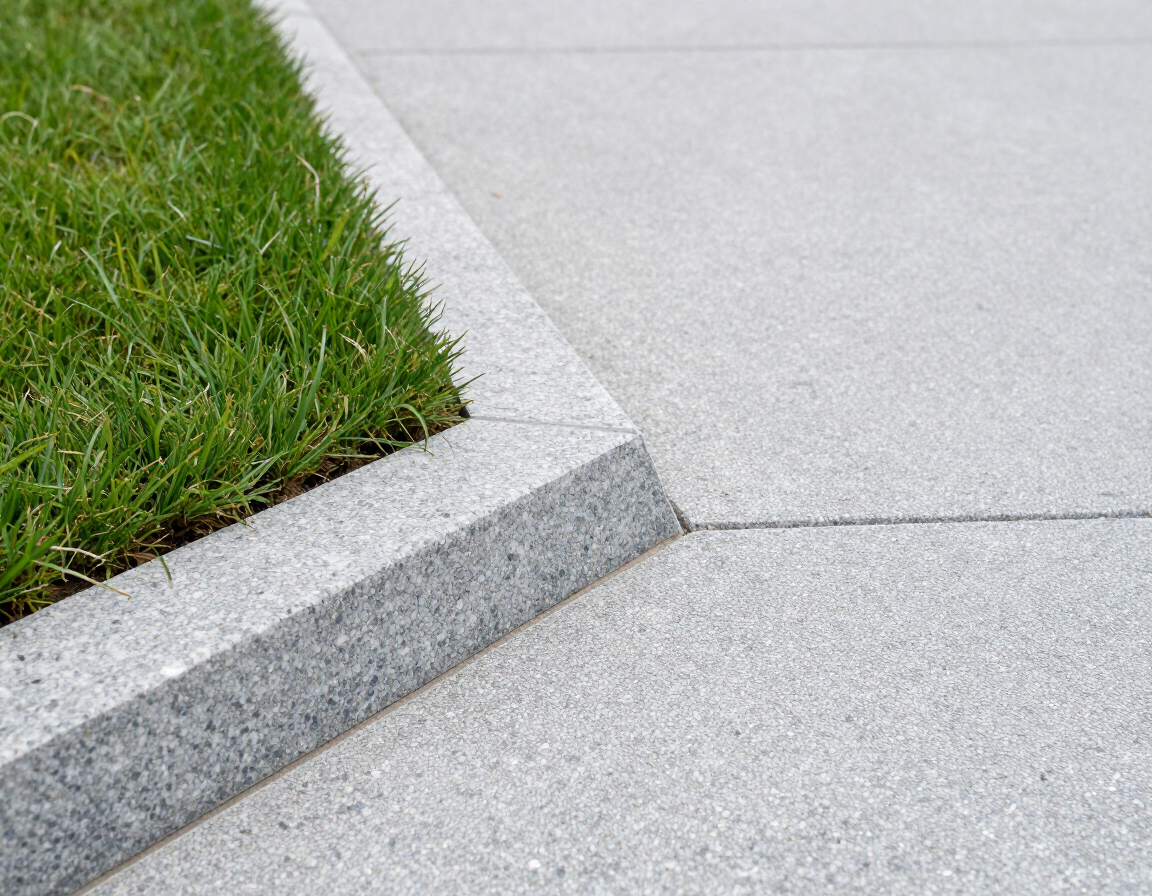 Concrete curb ramp beside green grass and a paved sidewalk corner