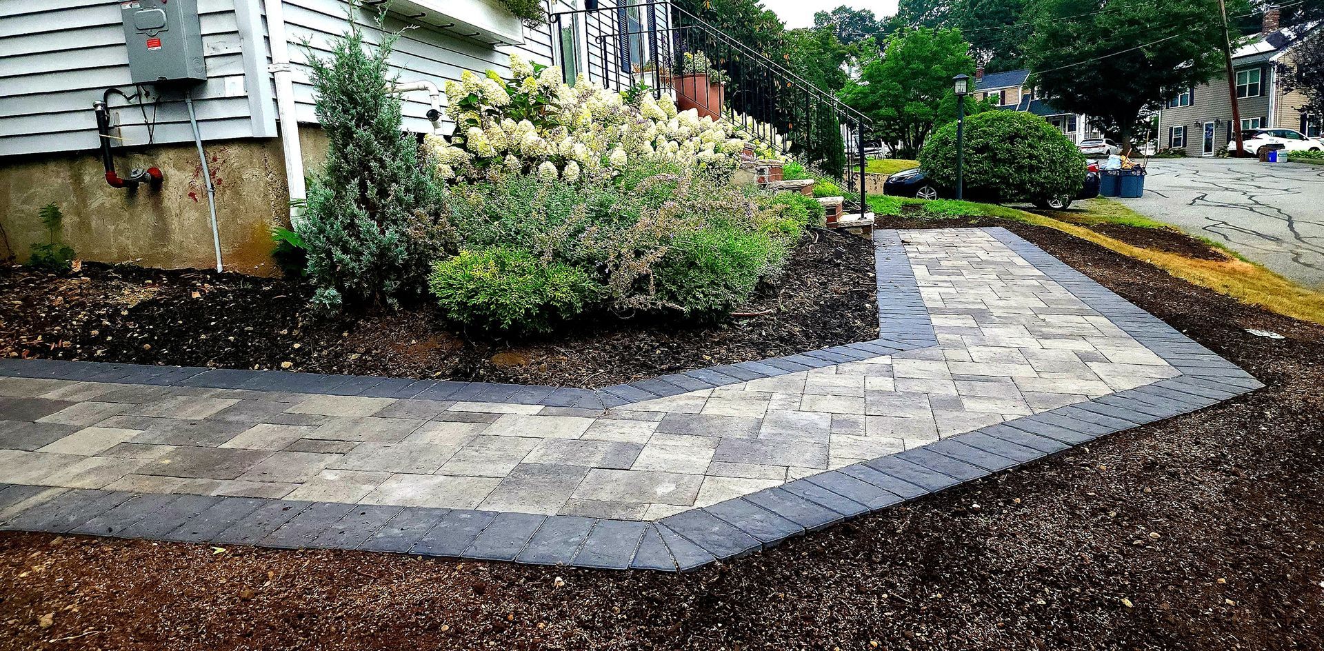 Paver walkway bordered by dark pavers, alongside a landscaped garden bed.